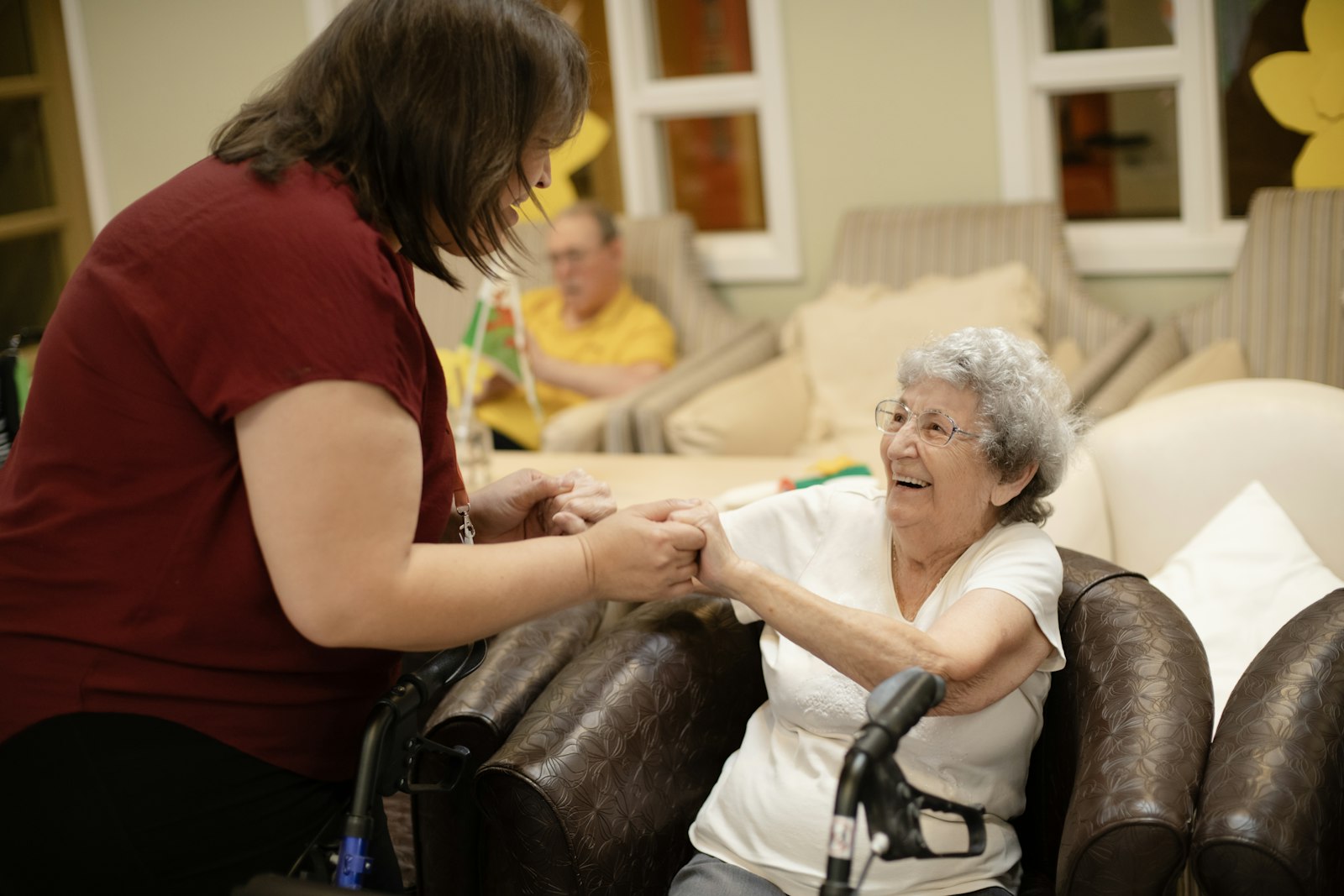 A caregiver warmly holding hands with a laughing senior client